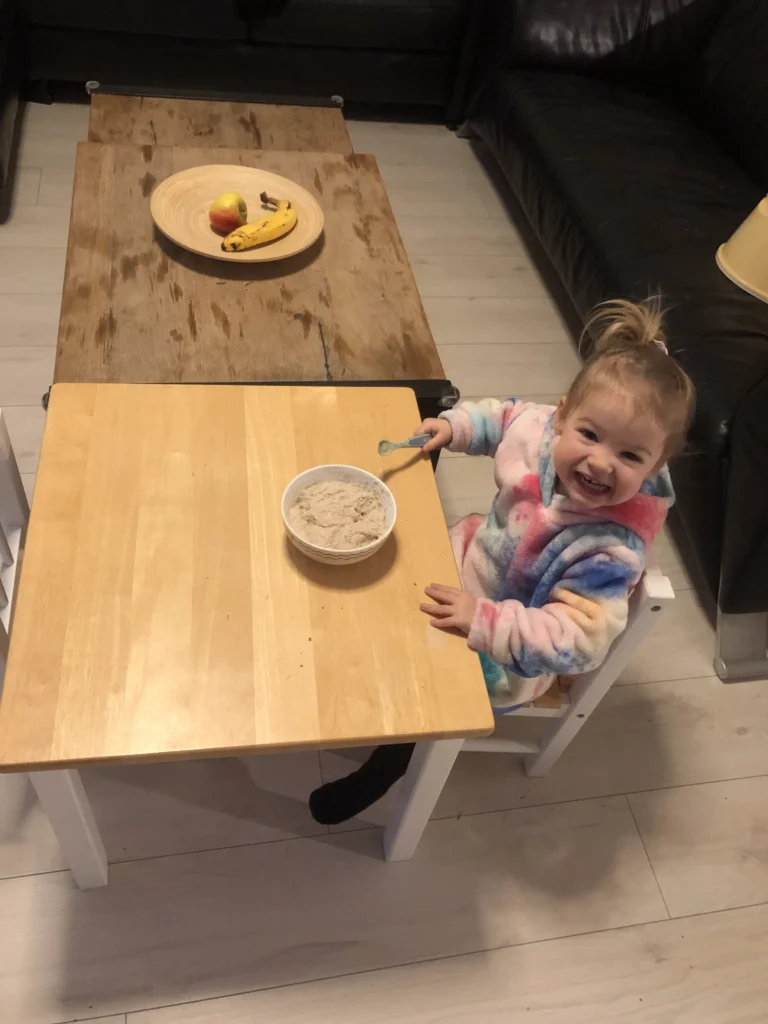 Peuter aan kindertafel met haar zelfgemaakte pap en een eigen fruitschaal