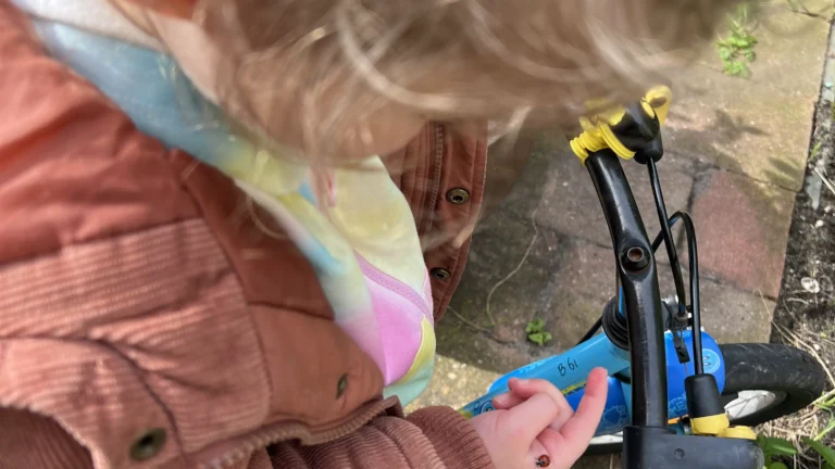 Peuter op fiets bestudeert lieveheerstbeestje op haar vinger